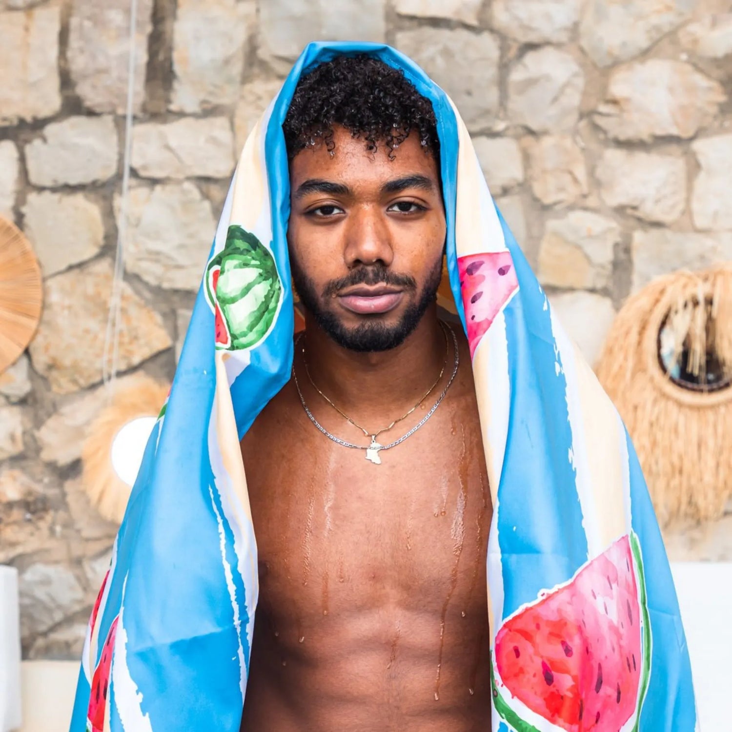 A guy putting a a Quick Dry, Sand Free, Light Weight, Compact and Ecofriendly Microfiber Beach Towel from La Toalla on his head with a watermelon design
