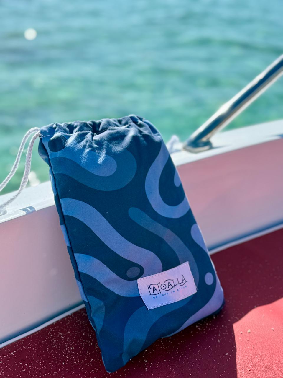 Blue drawstring bag with a La Toalla logo on a boat deck with water in the background