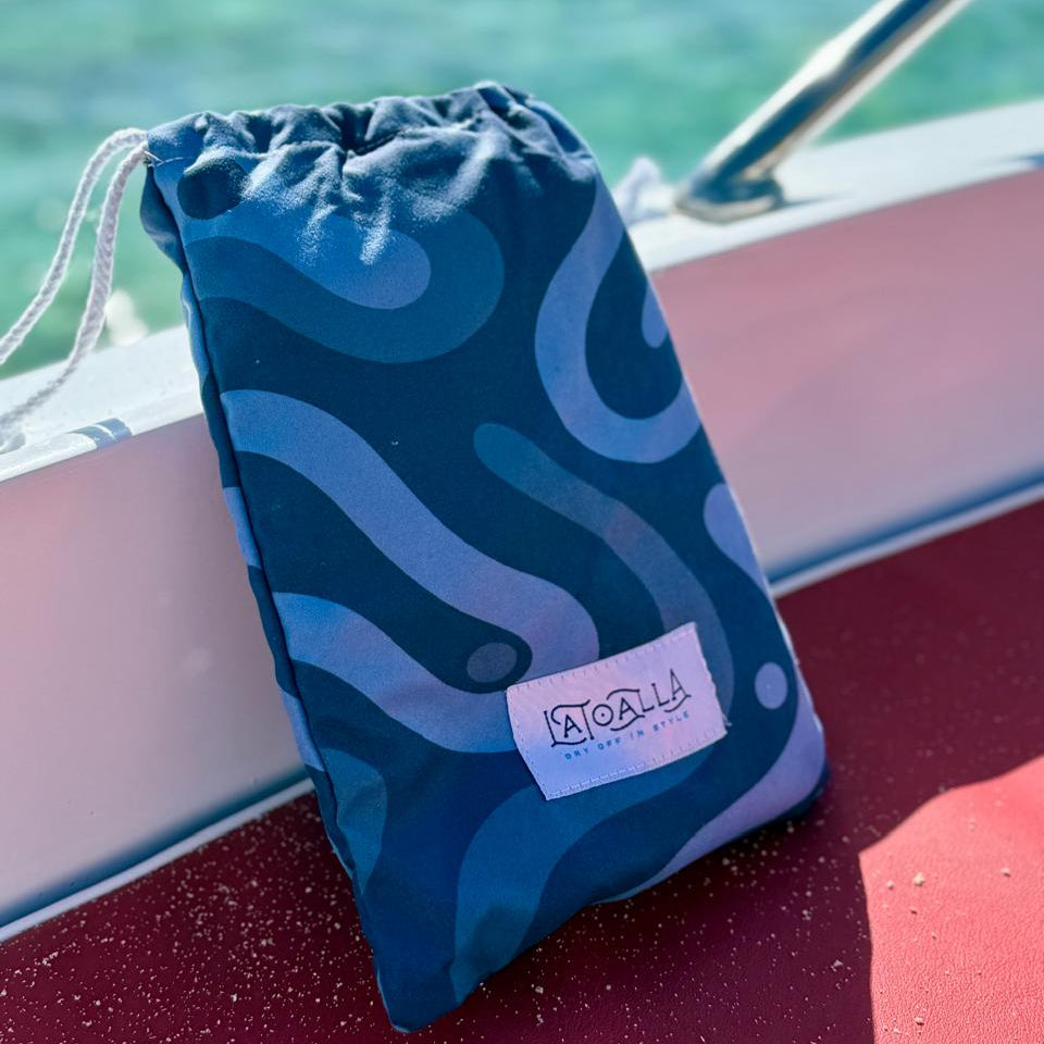 Blue drawstring bag with a La Toalla logo on a boat deck with water in the background