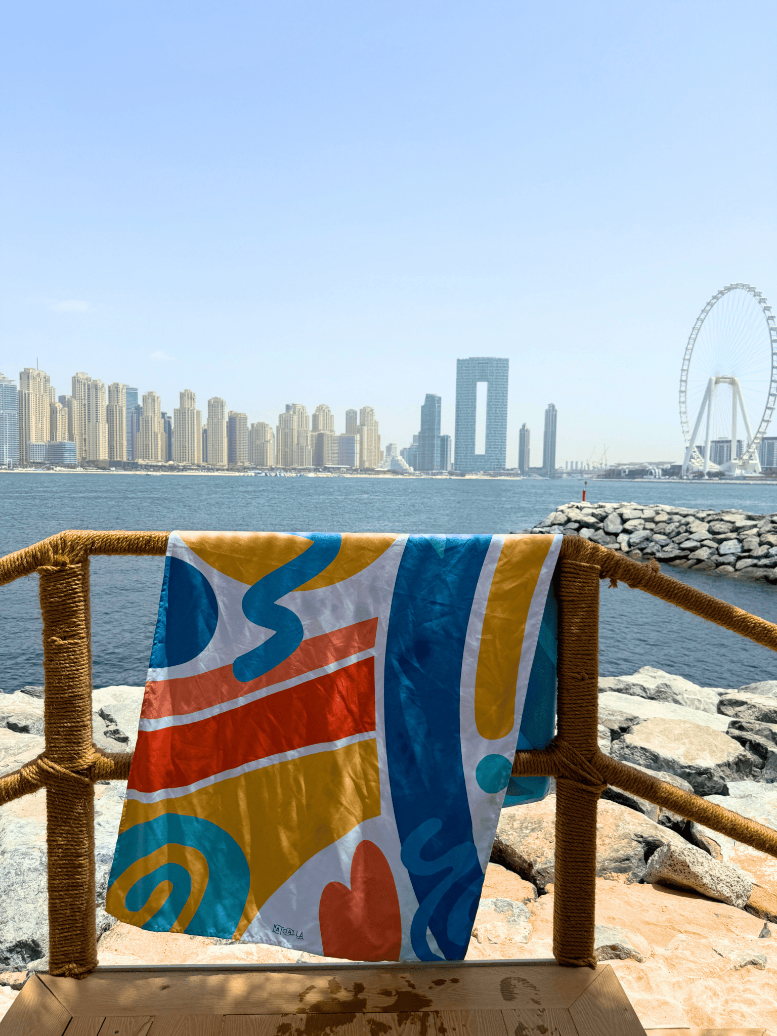Colorful towel with abstract patterns hanging on a railing by the water with city skyline in the background
