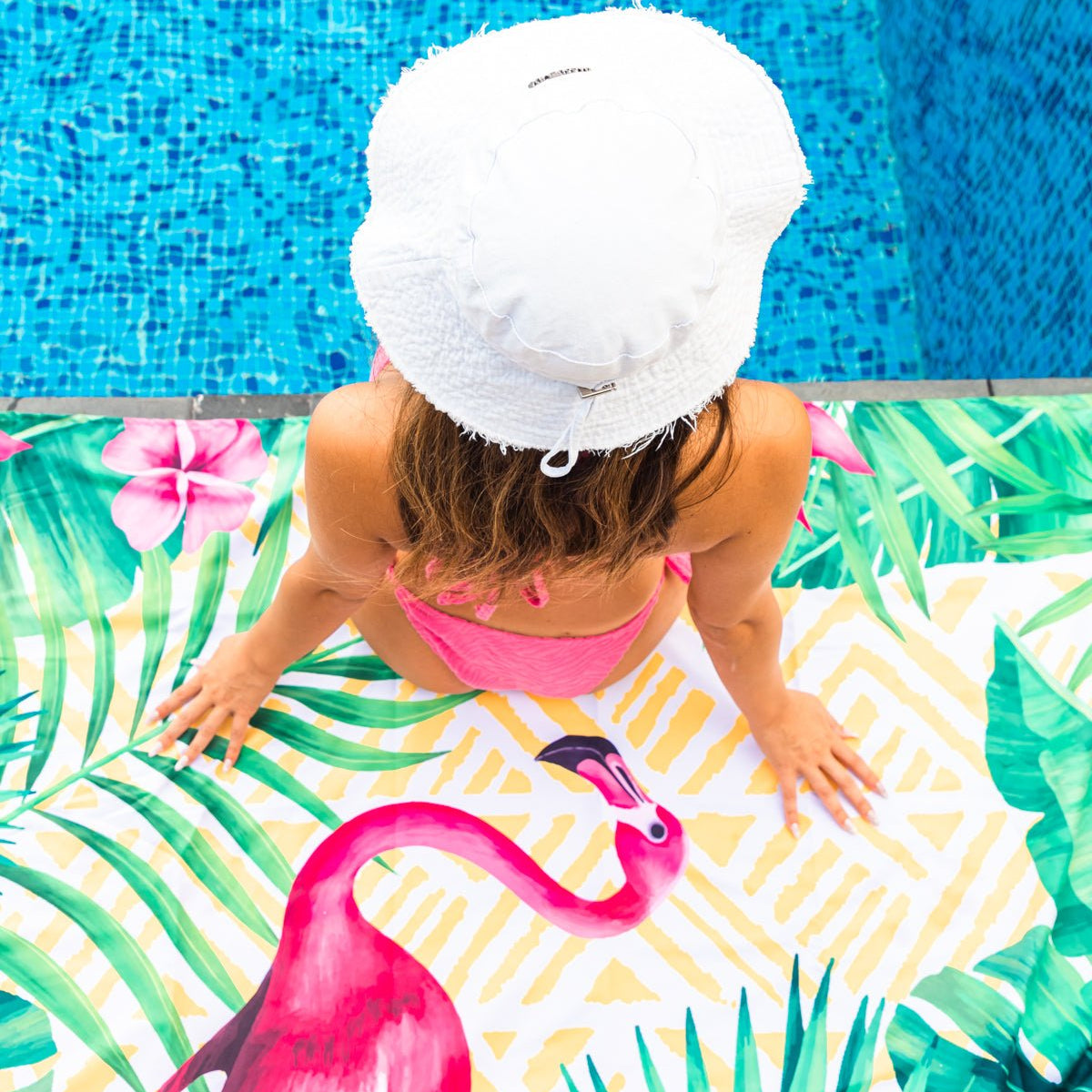 A girl sitting on the pool on a Quick Dry, Sand Free, Light Weight, Compact and Ecofriendly Microfiber Beach Towel from La Toalla